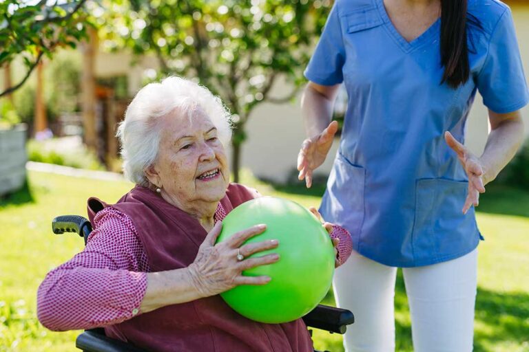 Caregiver sanitizing hands beside an older resident in a clean assisted living room